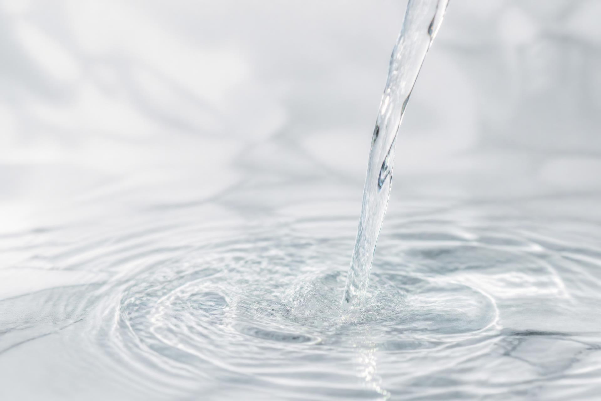 Crystal-clear water pouring into a calm pool with soft ripples